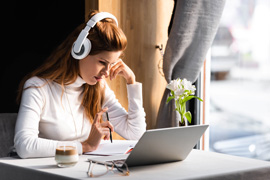 Woman wearing headphones watching a webinar on her laptop. Our on-demand resources include many recorded webinars and workshops.